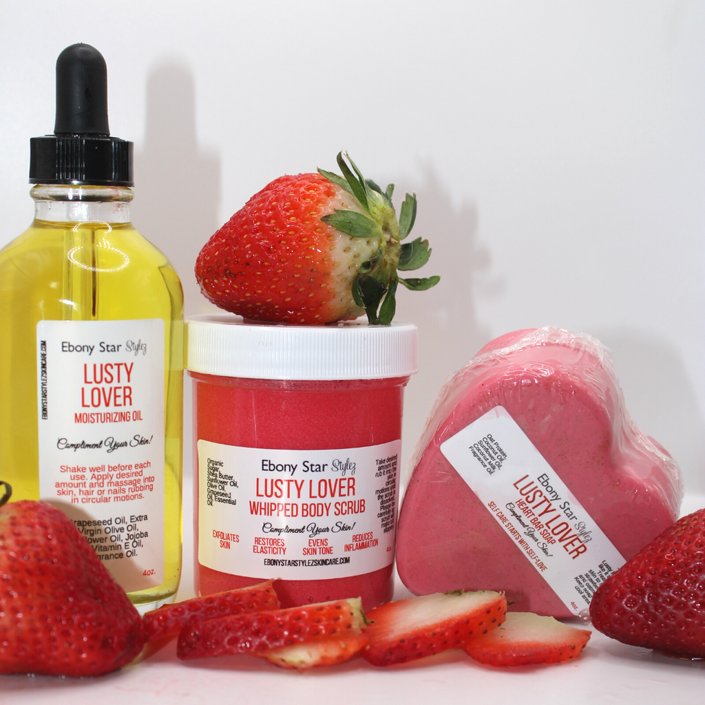 A body care bundle featuring a bottle of moisturizing body oil, a container of body scrub, and a bar of soap, all with a strawberry theme and branding details.